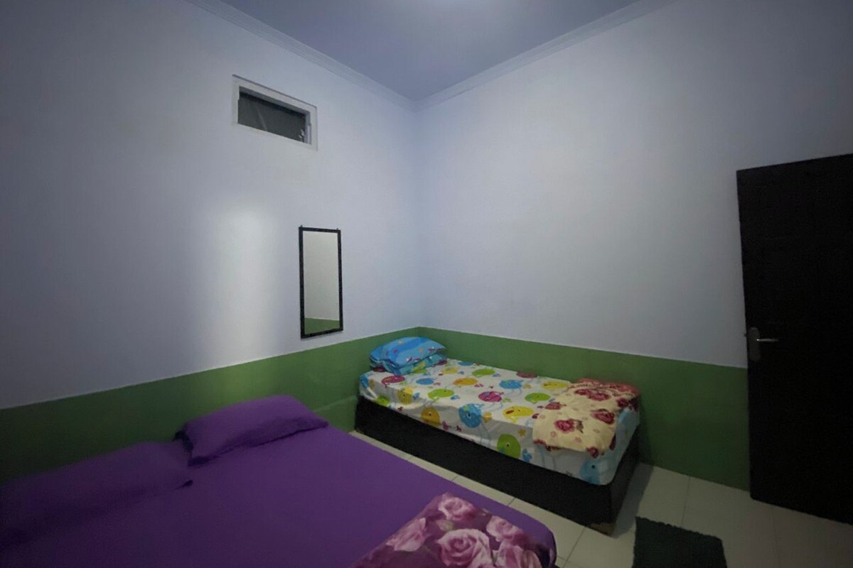 A small, single-bed room with a purple bedspread, a colorful bedspread, a small window, and a door.