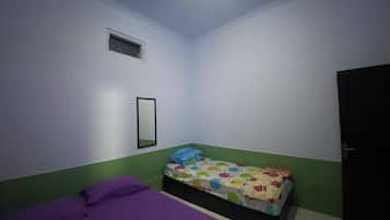 Una habitación pequeña con una cama individual, colcha morada, colcha colorida, una ventana pequeña y una puerta.