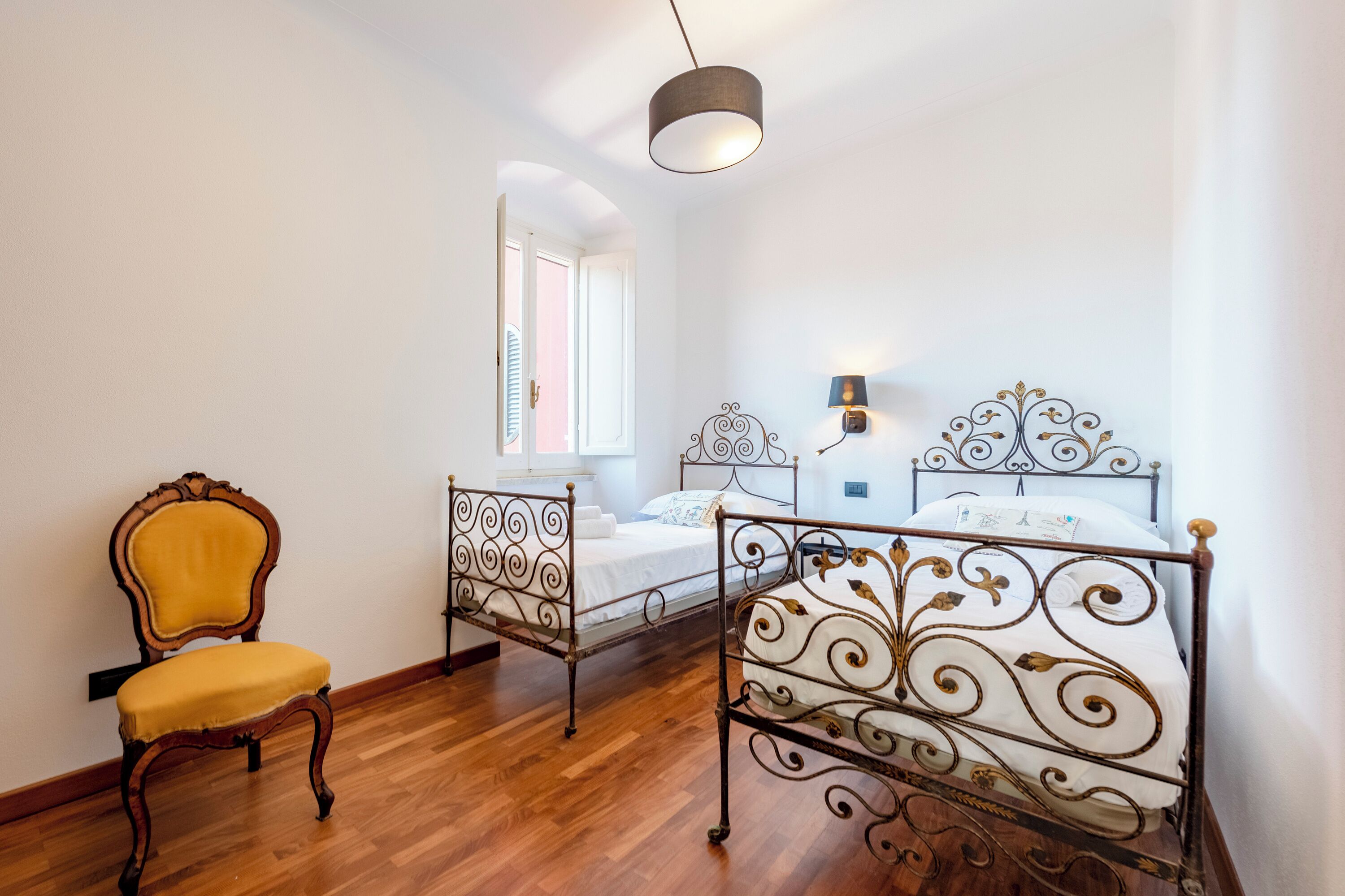 Une chambre à coucher avec deux lits en métal, une chaise en bois et un luminaire suspendu.