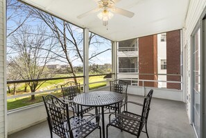 Une terrasse couverte avec une table ronde et des chaises, de grandes fenêtres et un ventilateur de plafond.