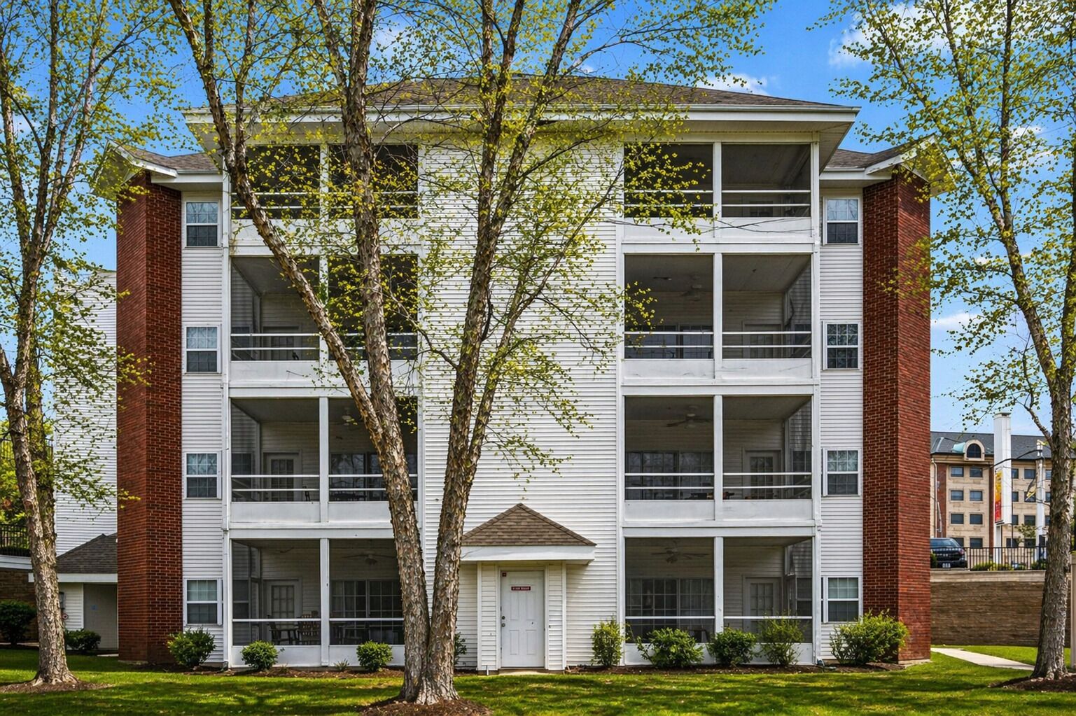 A multi-story apartment building with a central entrance, large windows, and a brick facade.