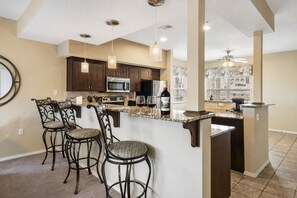 Una cocina con gabinetes de madera oscura, electrodomésticos de acero inoxidable, encimera de mármol e iluminación colgante.