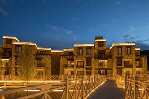 A stone building with multiple balconies and a wooden bridge over a reflective water body at night.