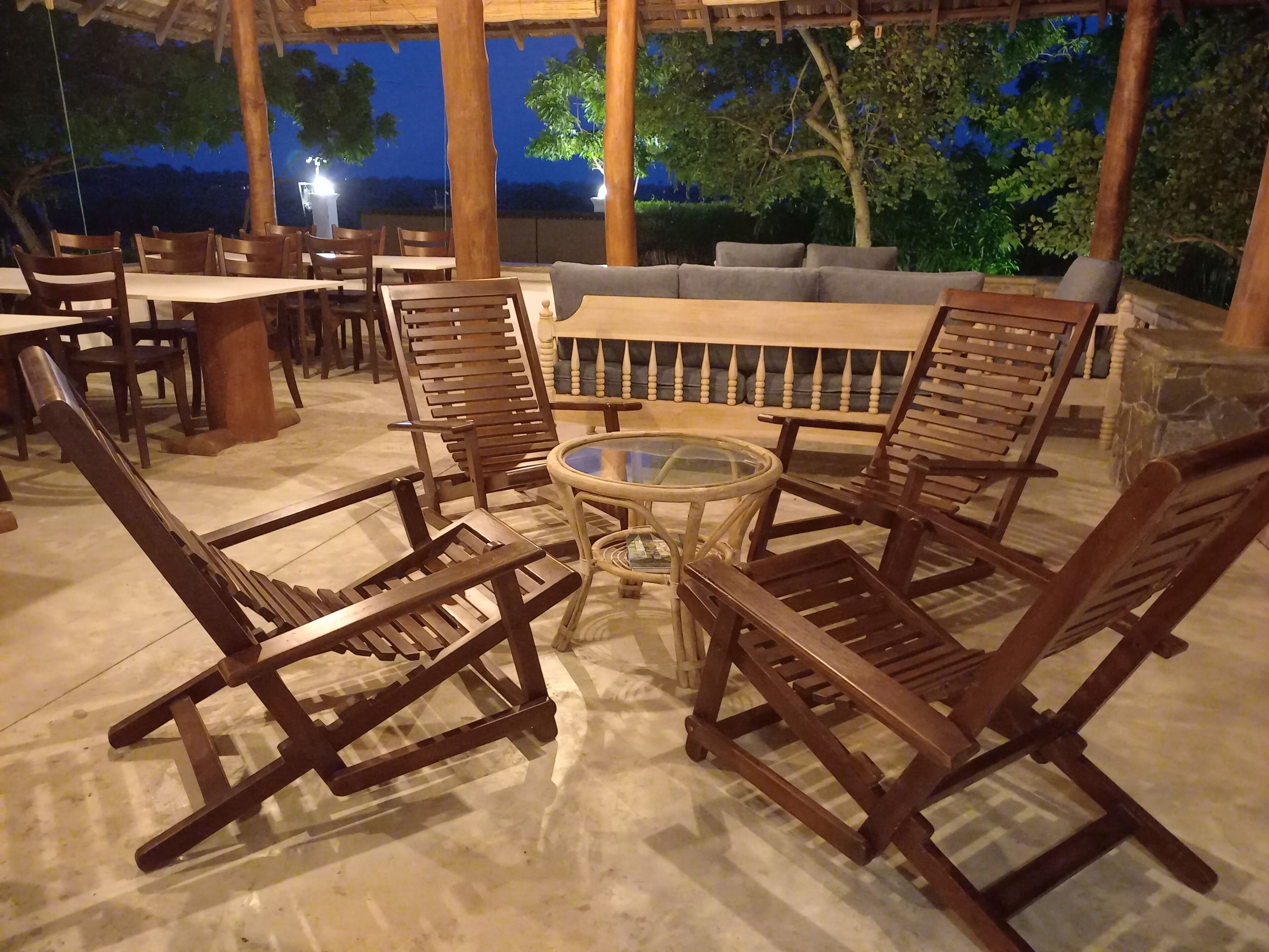 Un espacio al aire libre con sillas de madera y una mesa de vidrio, rodeado de pilares de piedra y una chimenea de piedra.