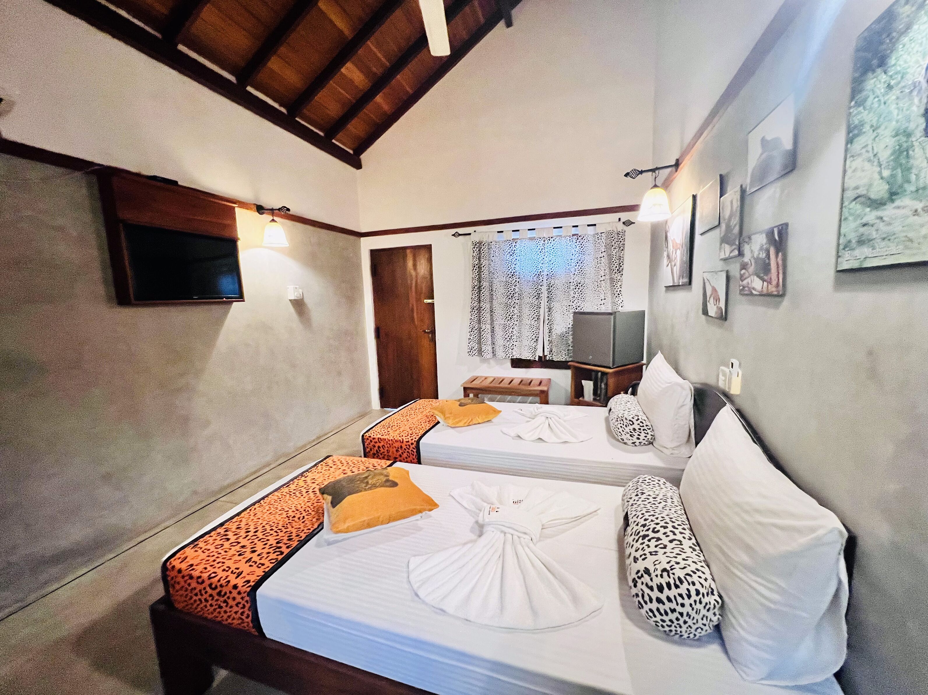 A hotel room with two beds, a TV, a desk, and a window with curtains.