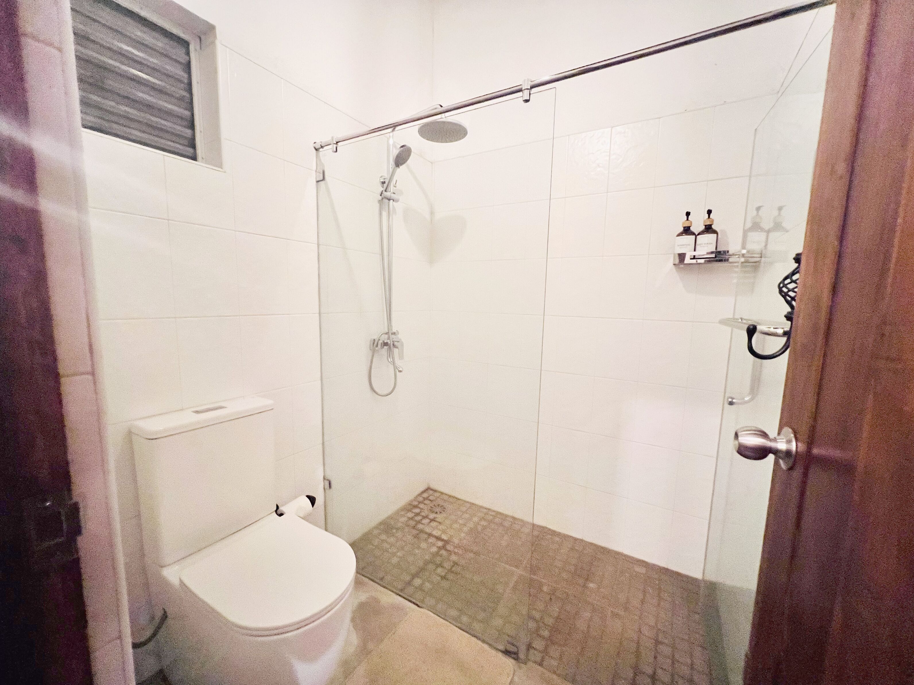 Un petit espace douche fermé, doté d’une porte en verre, de toilettes et d’un pommeau de douche.