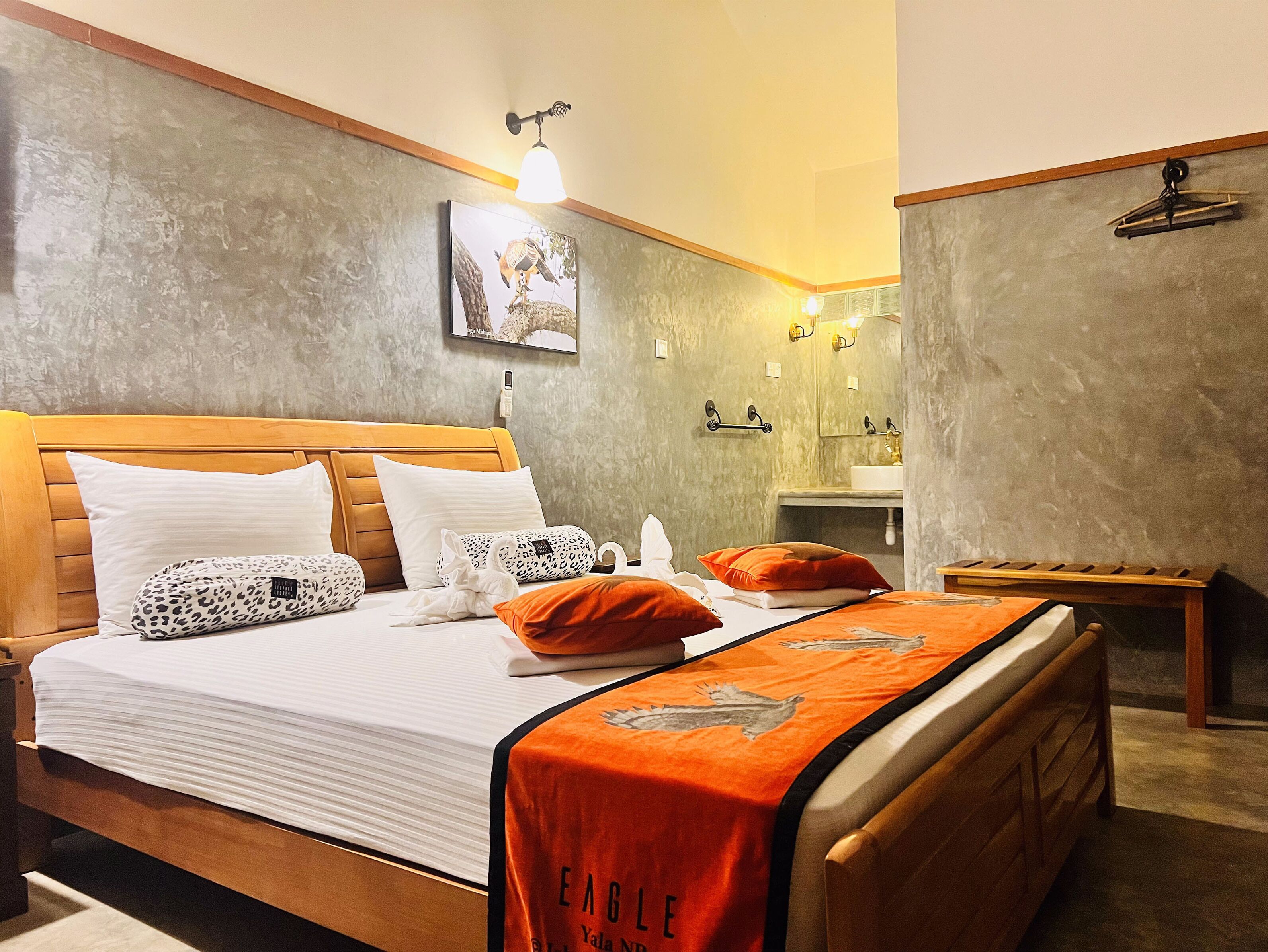 A hotel room with a wooden bed, white bedding, and a red blanket. There is a bathroom with a sink and a mirror.
