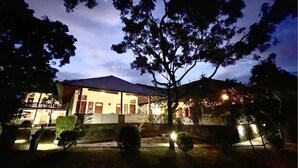 A two-story building with a covered patio area, surrounded by trees and a well-lit garden. - yala leopard lodge (Kirinda)