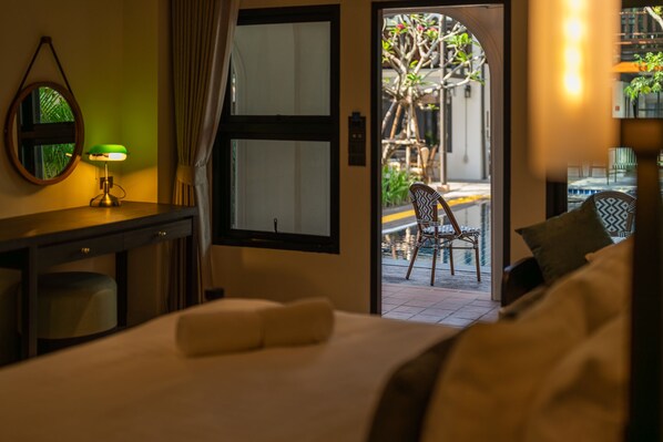 Une chambre d’hôtel avec un lit, un bureau doté d’une lampe, une chaise et une vue sur un espace extérieur comprenant un arbre et une piscine.