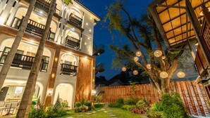 A multi-story hotel with balconies, a well-lit garden, and a large tree. - Shamrock Chiangmai Hotel - Adults Only (Chiang Mai)
