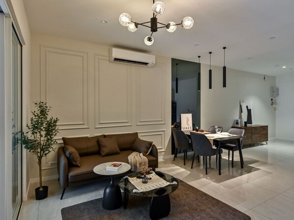 A modern living room with a brown sofa, a glass coffee table, and a dining area with a table and chairs.