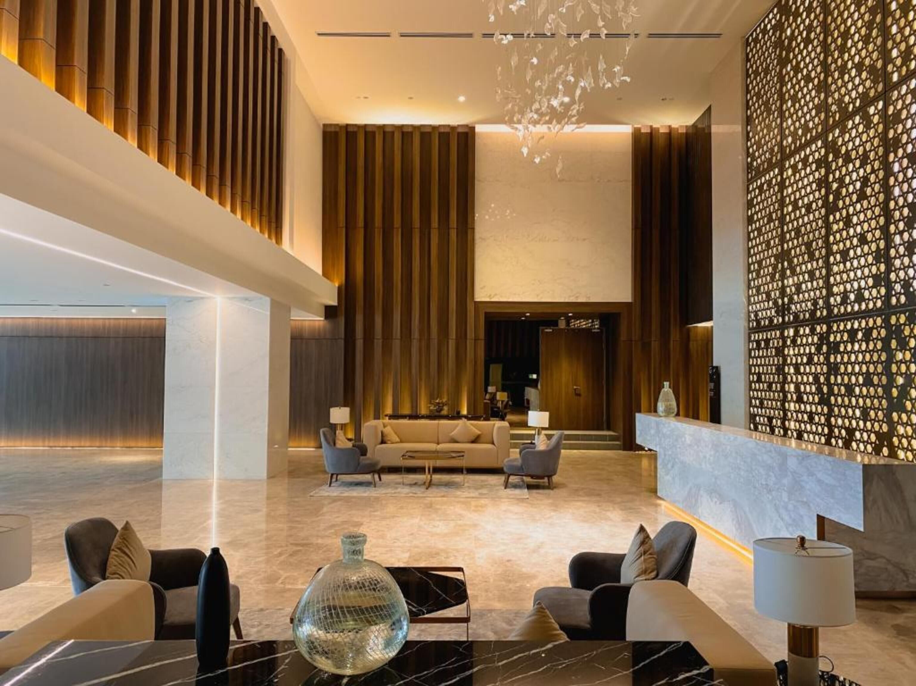A spacious lobby with a modern design, featuring a seating area with sofas and armchairs, a reception desk, and a decorative wall with a geometric pattern.