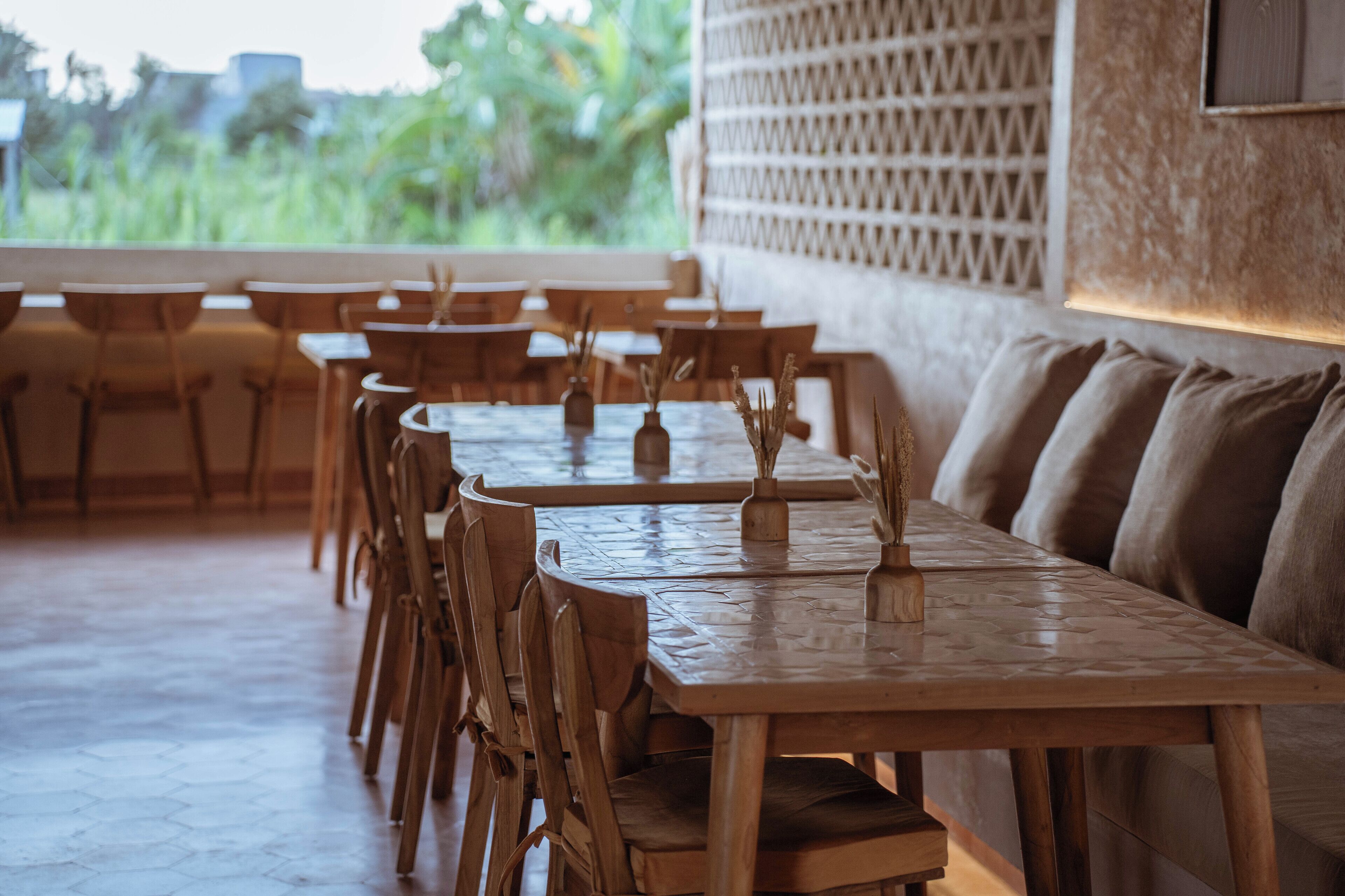 A restaurant with wooden tables and chairs, a patterned floor, and a view of greenery outside.