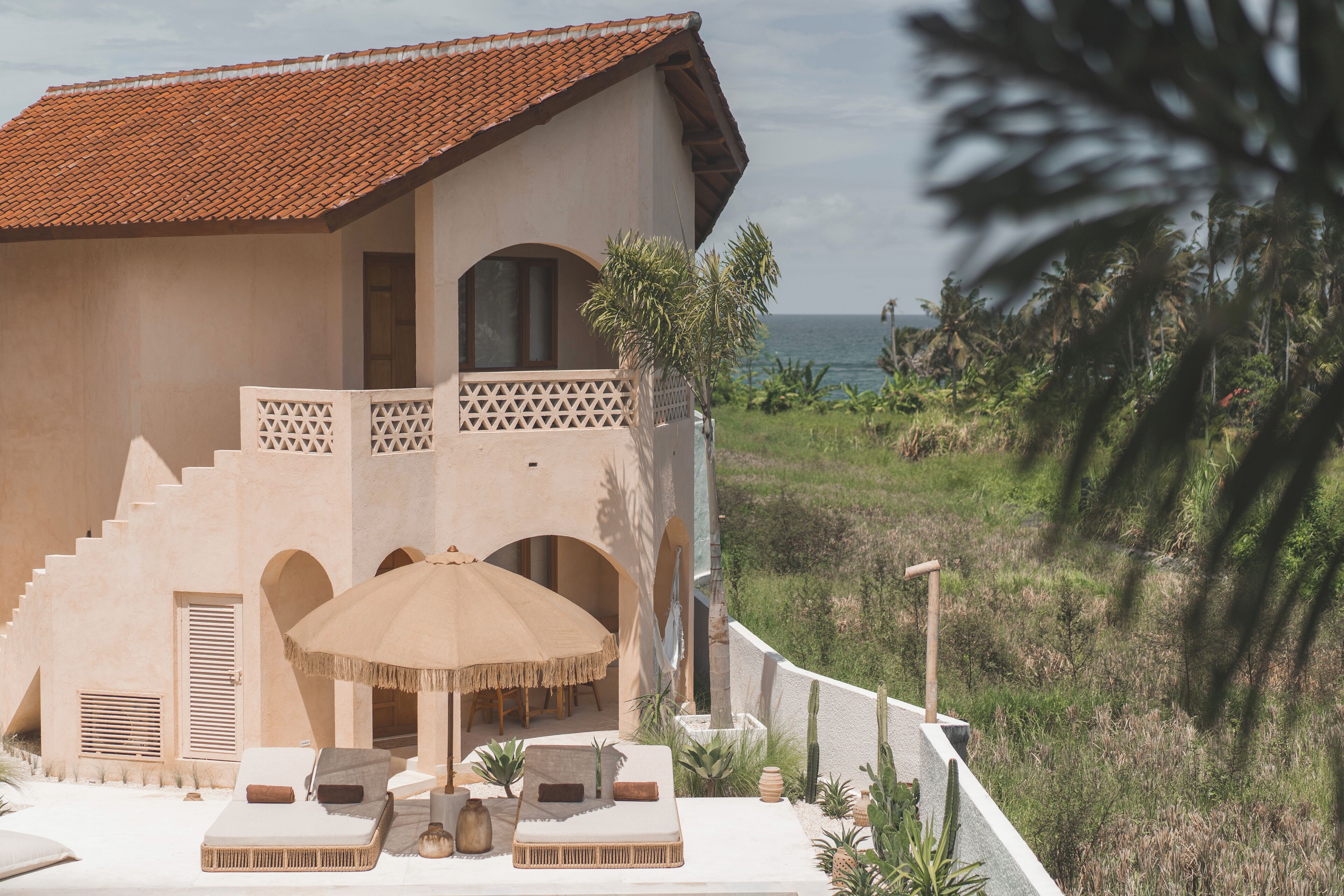 Une villa située en bord de mer, dotée d’une terrasse, de chaises longues et offrant une vue sur l’océan.