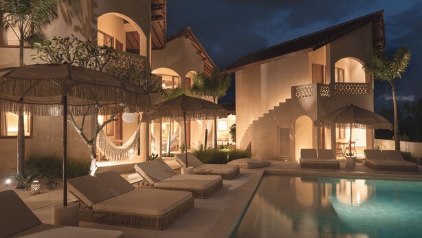 A poolside area with lounge chairs and umbrellas, a hammock, and a well-lit building with arched windows and balconies. - Dune Seseh (Cemagi)