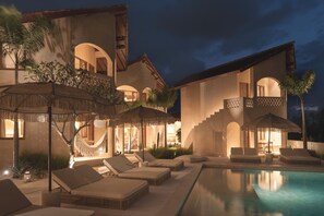 A poolside area with lounge chairs and umbrellas, a hammock, and a well-lit building with arched windows and balconies. - Dune Seseh (Cemagi)