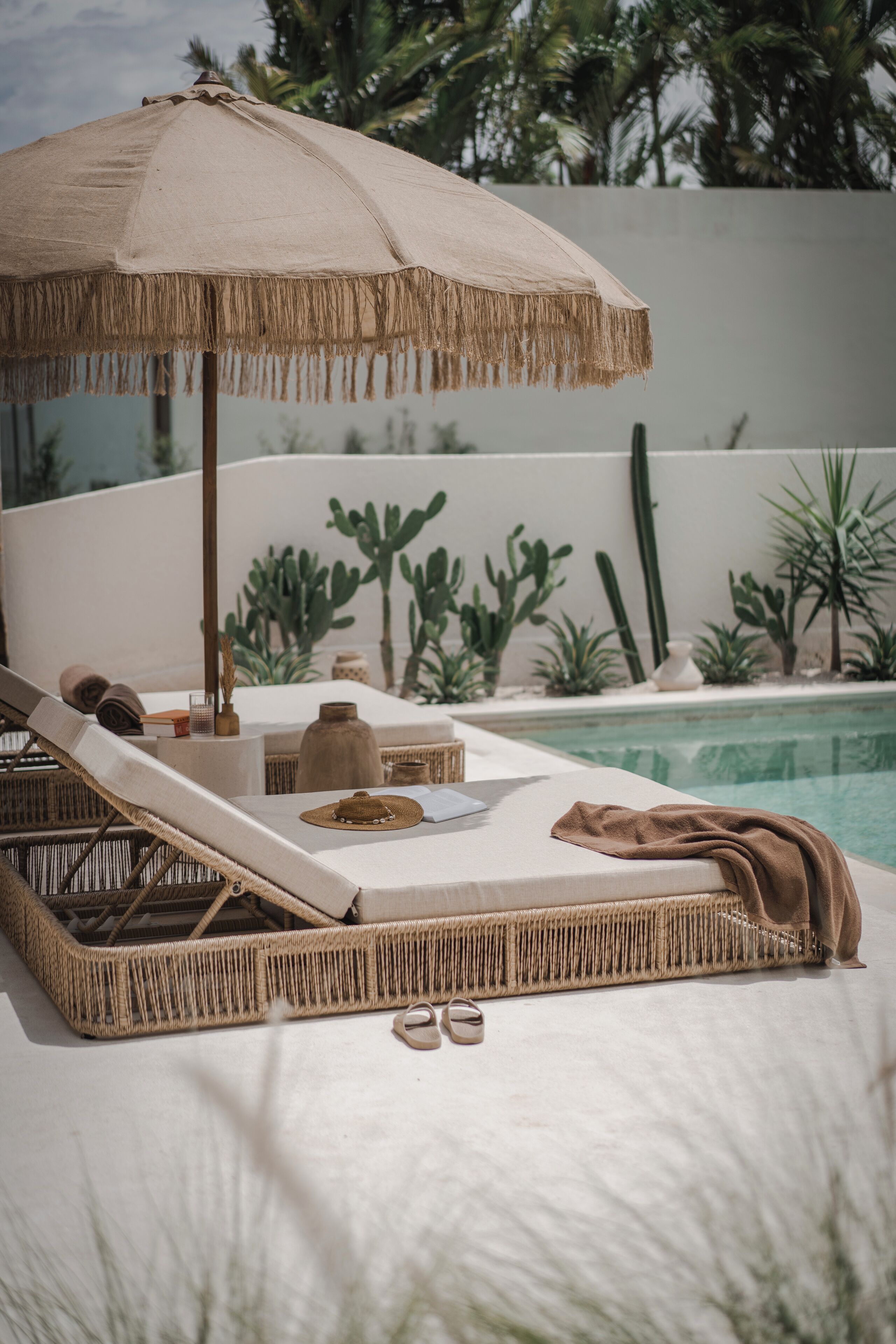 Une chaise longue avec un parasol en paille, une petite table et une paire de sandales.