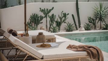 Une chaise longue avec un parasol en paille, une petite table et une paire de sandales.