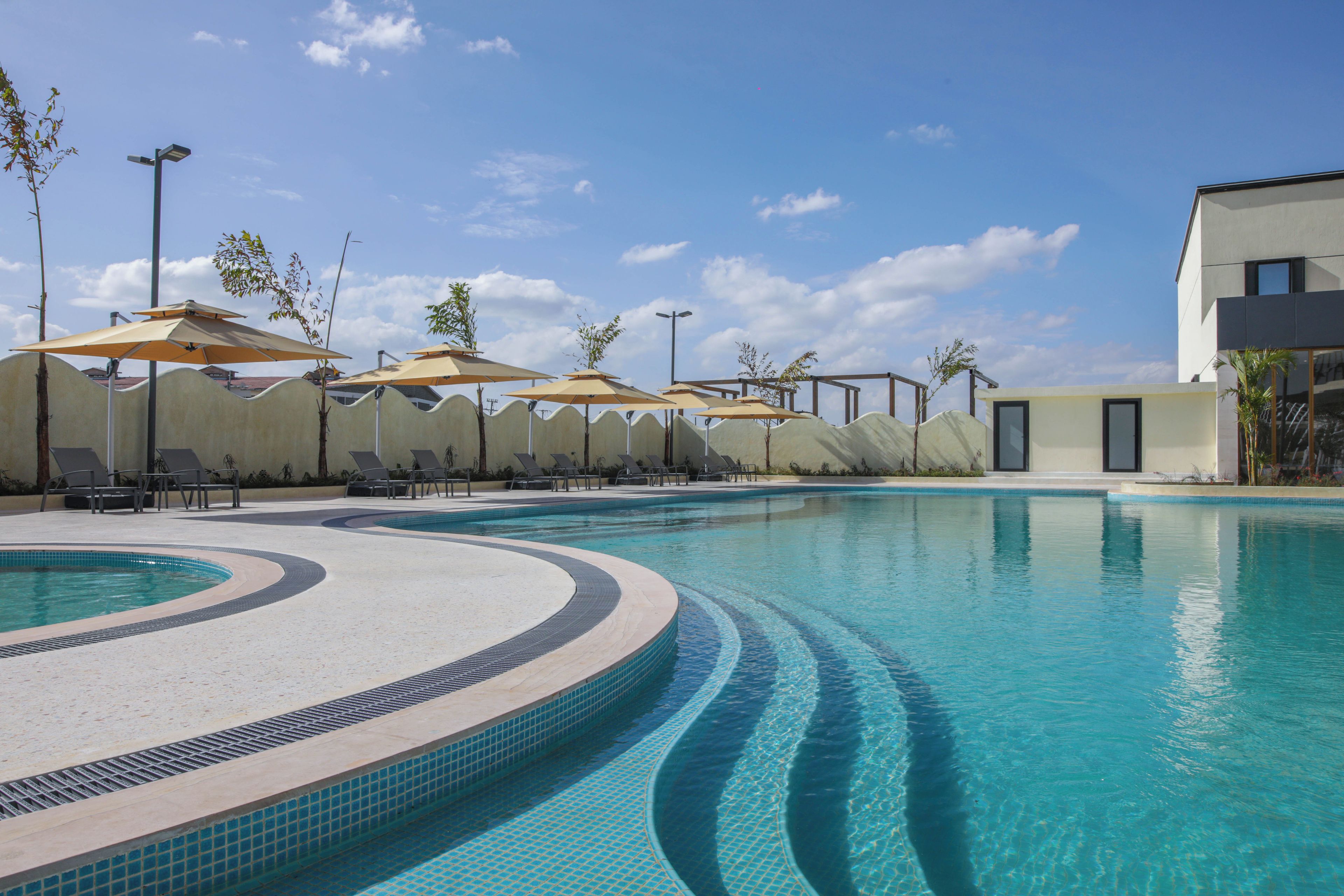 A swimming pool with lounge chairs and umbrellas, surrounded by a wavy wall and a building.