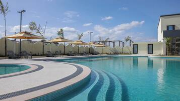 A swimming pool with lounge chairs and umbrellas, surrounded by a wavy wall and a building.