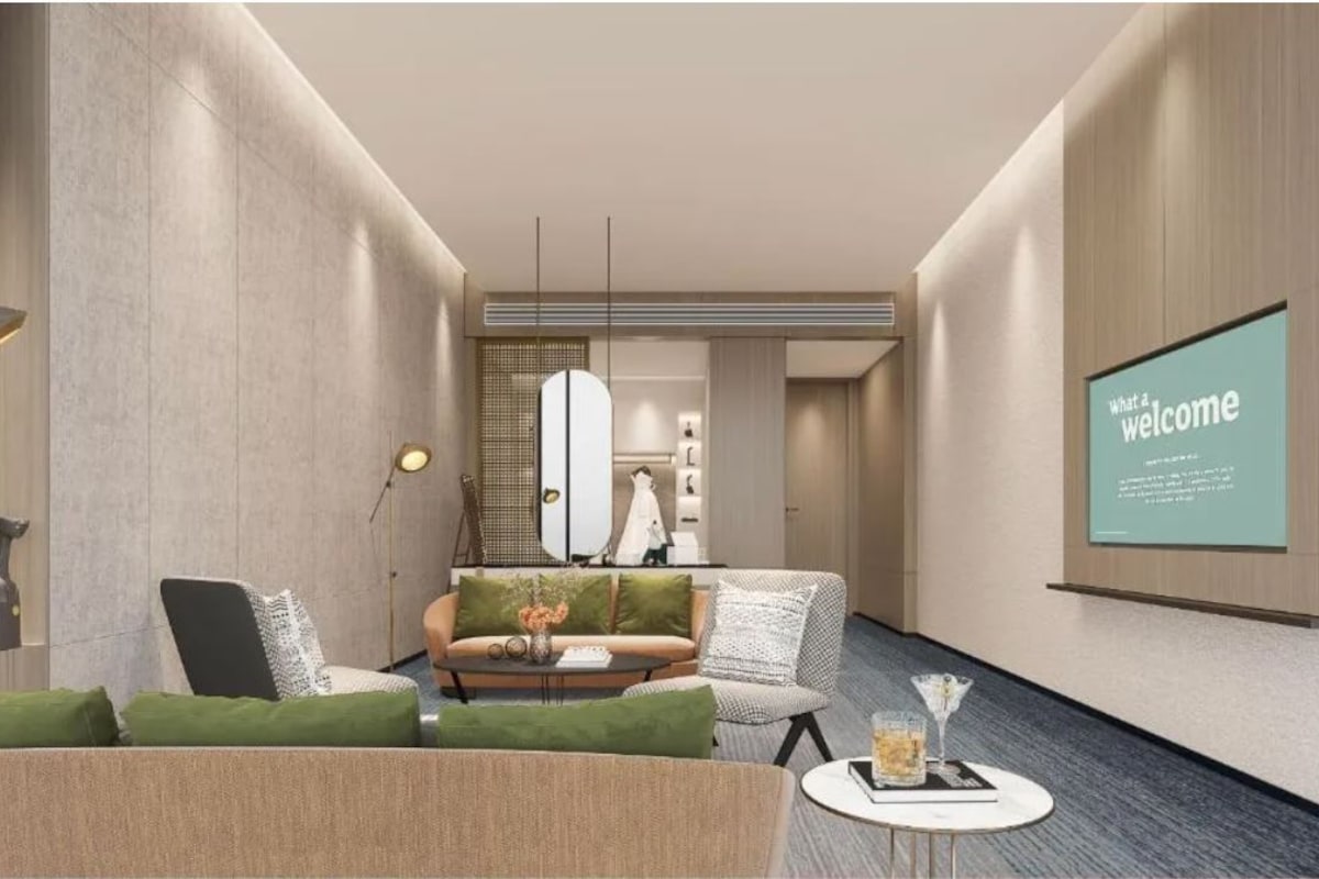 Een moderne hotellobby met een bank, fauteuils, een salontafel en een begroetingsscherm aan de muur.