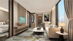 Ein modernes Hotelzimmer mit einem großen Bett, einer Couch, einem Couchtisch und einem Fernseher, der eine Willkommensnachricht anzeigt.