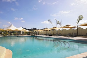 A swimming pool with lounge chairs and umbrellas, surrounded by a wavy wall and palm trees.