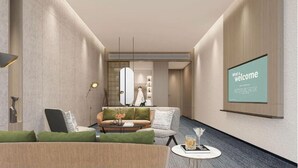 Eine moderne Hotelhalle mit einer Couch, Sesseln, einem Couchtisch und einem Willkommensbildschirm an der Wand.