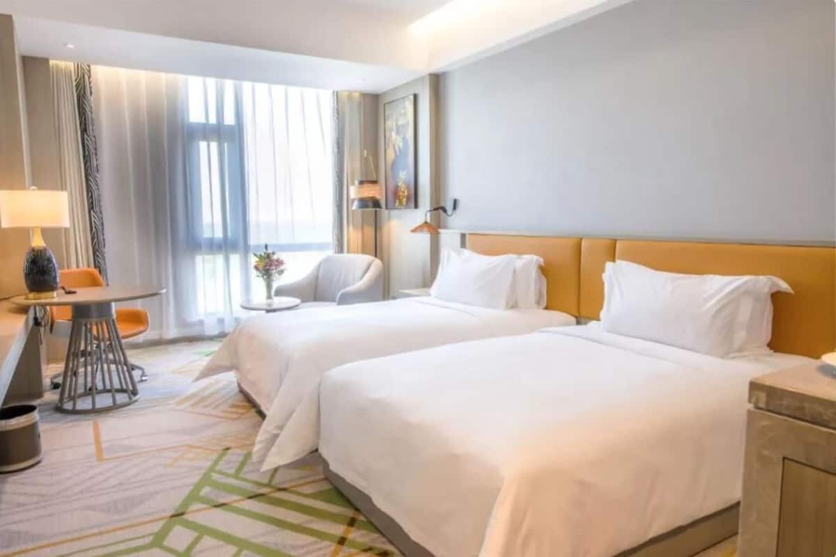Une chambre d’hôtel avec deux lits, un bureau, une chaise et une fenêtre avec des rideaux.