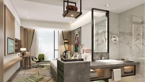 Una habitación de hotel moderna con una cama grande, una zona de estar con escritorio y silla, un espejo amplio, un baño con lavamanos y ducha de mármol, y un tapete con estampado verde.