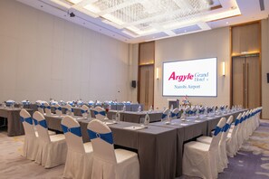 Un salón de conferencias con una larga mesa, sillas con cintas azules y una pantalla de proyector que muestra 'Argyle Grand Hotel Nairobi Airport'.