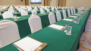 A conference room with rows of tables, each with a green tablecloth, white chairs, and water bottles.