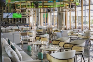 A modern lounge area with sofas, chairs, and tables, featuring a bar area with shelves and a television screen. - Argyle Grand Hotel (Syokimau)