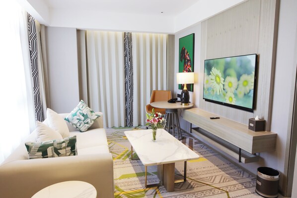 A modern hotel room with a sofa, a coffee table, a TV, a lamp, and a painting on the wall. - Argyle Grand Hotel (Syokimau)