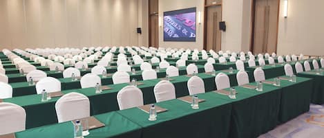 A conference room with rows of tables, each with a green tablecloth, white chairs, and water bottles.