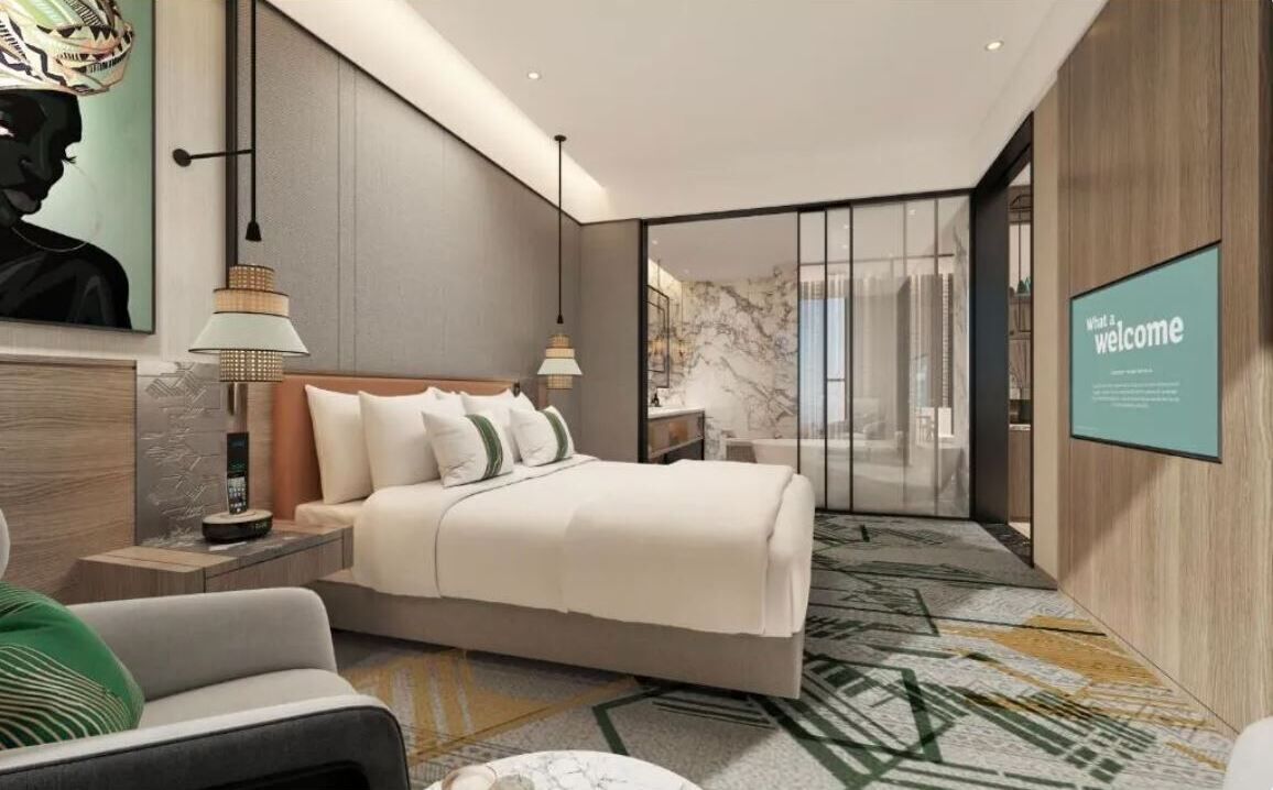 Quarto de hotel moderno com uma cama grande, mesas de cabeceira, uma escrivaninha e uma janela ampla.