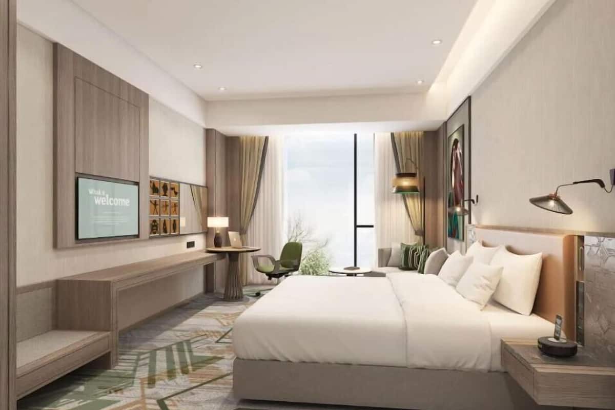 Une chambre d’hôtel moderne dotée d’un grand lit, d’un téléviseur fixé au mur, d’un bureau avec une lampe et offrant une vue sur l’extérieur.