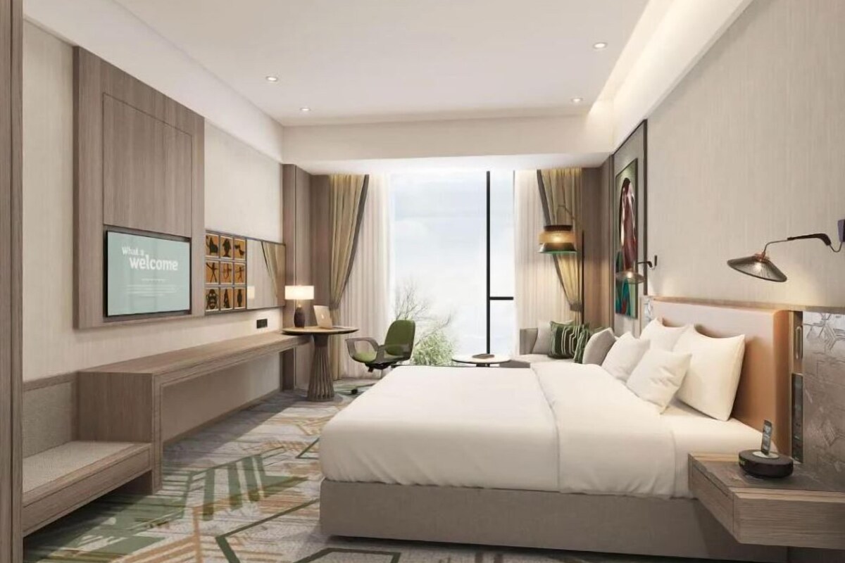 Un hotel moderno con una cama grande, un televisor montado en la pared, un escritorio con lámpara y vistas al exterior.