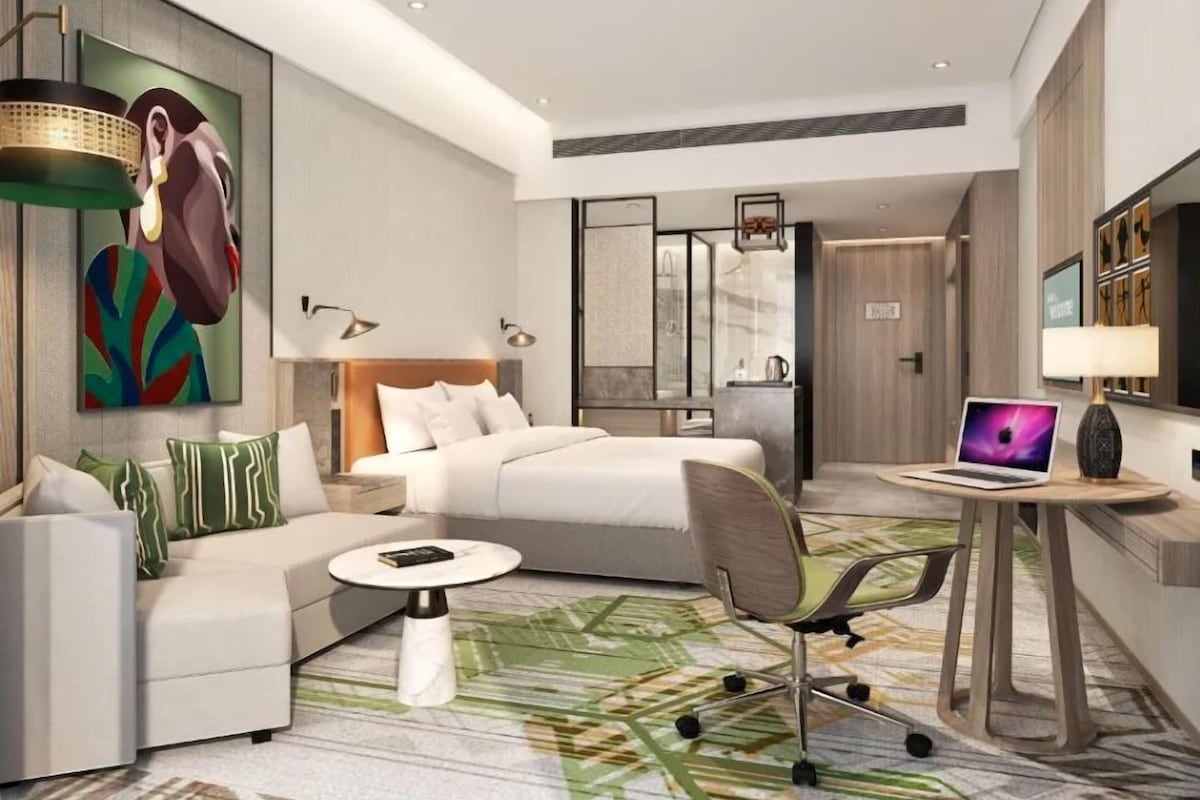 Una habitación de hotel moderna con una cama, un sofá, un escritorio con una computadora portátil y un cuadro en la pared.