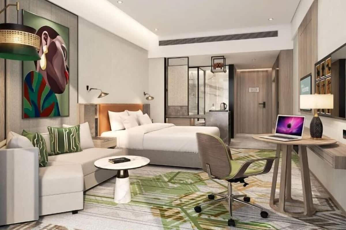 Une chambre d’hôtel moderne, équipée d’un lit, d’un canapé, d’un bureau avec un ordinateur portable et d’un tableau au mur.