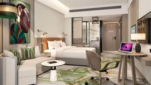 Una habitación de hotel moderna con cama, sofá, escritorio con una computadora portátil y un cuadro en la pared.