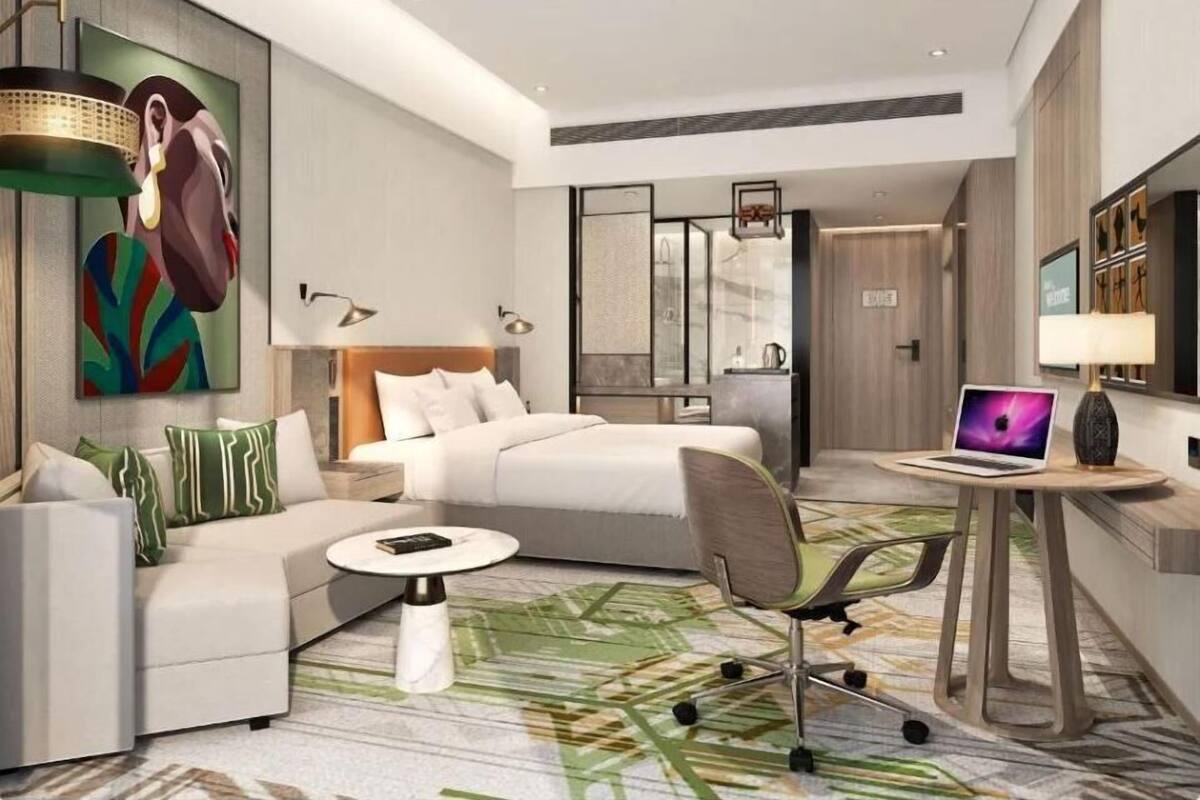 Une chambre d’hôtel moderne, équipée d’un lit, d’un canapé, d’un bureau avec un ordinateur portable et d’un grand tableau accroché au mur.