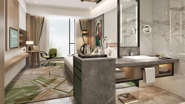 Ein modernes Hotelzimmer mit einem großen Bett, einer Sitzecke mit Schreibtisch und Stuhl, einem großen Spiegel, einem Badezimmer mit Marmorwaschbecken und Dusche sowie einem grün gemusterten Teppich.