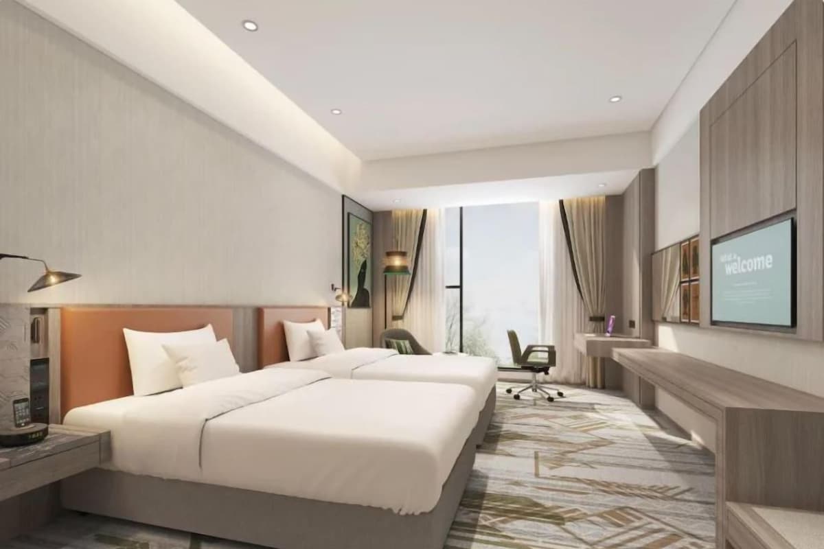 Habitació d'hotel moderna amb dos llits, escriptori, cadira i una finestra gran.