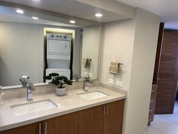 Une salle de bain moderne avec deux vasques, un grand miroir et une plante en pot.