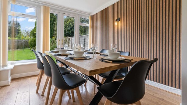 A dining area with a wooden table set for four, black chairs, and a large window with a view of greenery. - 3 Bedroom Home Sleeps 7 OR 8 Free Parking NR Solihull Edgbaston and City Centre (Birmingham)