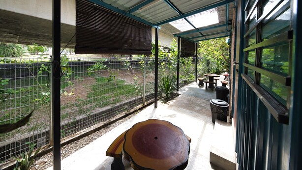 Un espacio al aire libre techado con suelo de hormigón, una mesa grande de madera y una valla metálica.