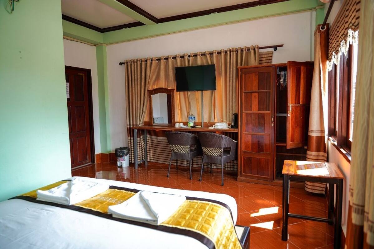 A hotel room with a bed, a desk, two chairs, a television, and a wardrobe.