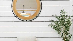 A wooden console table with storage compartments, a round mirror with a black frame, and a potted plant.