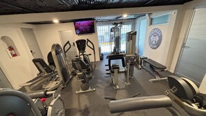 A gym with cardio machines, weightlifting equipment, and a TV screen displaying a workout video. - Vidalia 3 - New Condo with Gym and Rooftop Terrace with Jacuzzi (Puerto Vallarta)